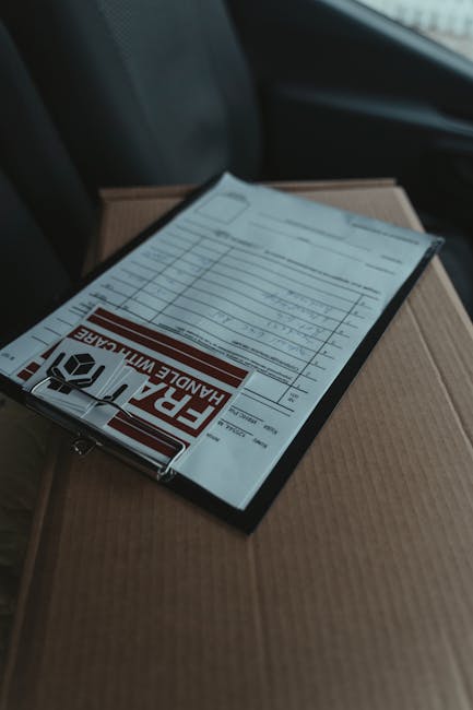 A close-up of a delivery parcel with a floral order receipt placed on top, resting on a cardboard box. The receipt displays details of a flower order, with a bold red and white 'Fragile Handle With Ca