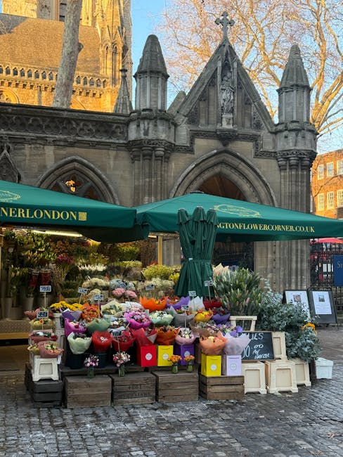 A vibrant flower stall situated outdoors in front of historic Gothic-style architecture with pointed arches and decorative stonework, featuring an array of fresh flowers including pink, purple, yellow