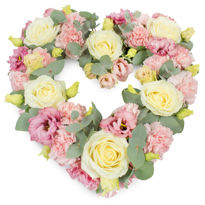 A full, heart-shaped wreath of pastel flowers is set against a clean white backdrop, presenting a serene, deeply personal funeral tribute that would feel entirely at home in a South Hackney church, crematorium, or family flat. The heart is lavishly filled with creamy ivory and light yellow roses, each rose carefully positioned so that its velvety, spiralling petals are fully visible, creating a luxurious base of soft, rounded forms. Interwoven with these roses, clusters of delicate pastel pink carnations add volume and feathery texture, their many tiny petals curling and overlapping like folds of fine fabric, lending a gentle, comforting softness to the whole composition. Richer tones emerge where magenta-pink and mauve lisianthus blossoms appear, some fully open with fluted, trumpet-like petals, others just beginning to unfurl, contributing a sense of depth and quiet emotion reminiscent of sunset skies over nearby London Fields. Eucalyptus foliage loops gracefully through the design, its cool, silvery-green leaves offering a modern, calming contrast to the warm pastels, while also framing the heart's contour with understated elegance. Tiny yellow-green buds are scattered throughout, fresh and tightly closed, symbolizing the unbroken thread of life even in times of parting. The pure white background ensures the heart's shape is immediately recognizable, underscoring its message of enduring love, remembrance, and sympathy. Created with the care of an experienced South Hackney florist, this wreath would make a thoughtful tribute for a funeral service, burial, or memorial gathering, quietly conveying respect, affection, and shared grief for someone dearly missed.
