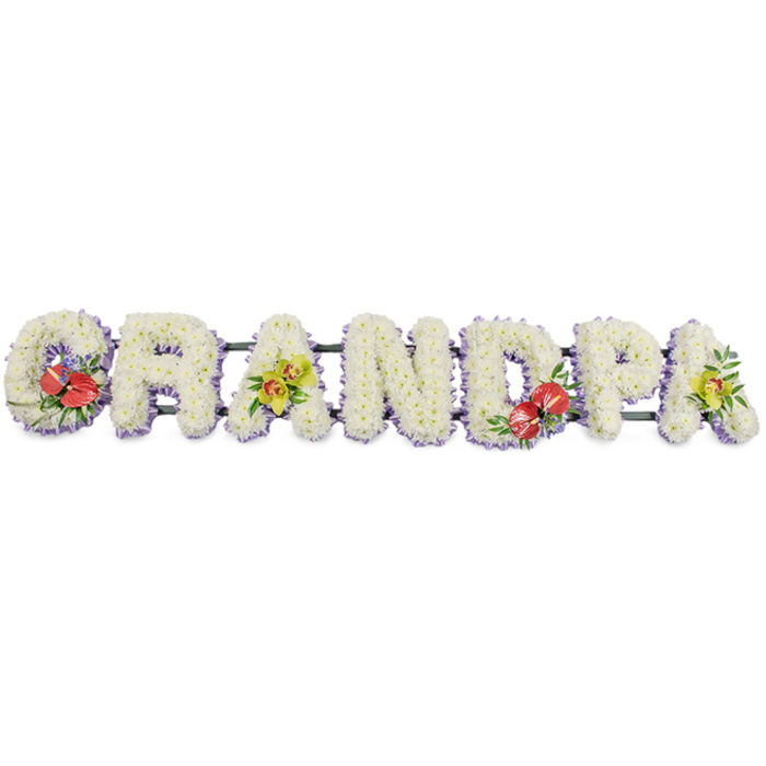 This image shows a striking GRANDPA funeral flower tribute, arranged in bold capital letters that run horizontally across the frame. Each letter is three-dimensional and generously covered with fresh white chrysanthemums, placed so closely that they create a smooth yet textured surface, like a soft floral tapestry. The blooms are uniform in size and tone, giving the tribute a clean, peaceful appearance that feels appropriate for a church service or crematorium gathering in South Hackney. Along the base of every letter, a slim strip of light purple ribbon is just visible beneath the flowers, lending a gentle lavender glow that outlines the shapes and brings a touch of refinement. Behind the scenes, dark green connecting rails hold the letters in line, giving the design enough structure to be displayed by the coffin or at the front of a chapel near London Fields or along Mare Street. Richly coloured accent sprays bring the tribute to life. The G and the D feature clusters of deep red anthuriums, their heart-shaped, waxy petals and prominent yellow spadices standing out vividly against the white chrysanthemum background, framed by deep green leaves and a few subtle touches of complementary filler. The first and last A are decorated with clusters of yellow-green orchids, their elegant blooms and gently arching stems threaded among glossy foliage, adding sophistication and a contemporary feel. The tribute reads clearly and feels very personal, a bespoke floral arrangement created for a beloved grandfather whose memory is being honoured by family and friends in South Hackney with fresh, beautifully arranged flowers.