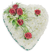 A serene, heart-shaped funeral tribute composed entirely of hundreds of small, pristine white chrysanthemums rests against a clean white background, the overall effect one of cloud-like softness and quiet dignity. The chrysanthemum cushion is densely packed so each blossom contributes to a continuous, velvety surface that suggests purity and remembrance. From the upper left a cluster of three deep red roses gathers close together, their fully opened petals presenting a rich, velvety crimson that reads as love, respect, and deep sorrow. Lush green foliage - glossy ruscus leaves and delicate, fern-like fronds - nestles these three roses and sends out a few slender blades of bear grass that arc gently across the white field, introducing movement and a subtle architectural line. Two further red roses punctuate the design: one sits near the upper right curve of the heart and another marks the bottom point, each given a small halo of green sprigs so they read as solitary, reverent moments of reflection. A narrow emerald green satin ribbon trims the heart's edge, neatly defining the silhouette and adding a calm, traditional finish. Soft overhead lighting brings out the texture of the chrysanthemum bed and throws faint shadows beneath the leaves, emphasizing depth without distraction. As you might see at a South Hackney funeral or placed near a chapel in Victoria Park or on a service table by Mare Street, this arrangement conveys composed sympathy, heartfelt condolences, and a respectful farewell. The composition and scent combine to offer comfort - an elegant, time-honoured emblem of remembrance crafted with mindful floral technique.